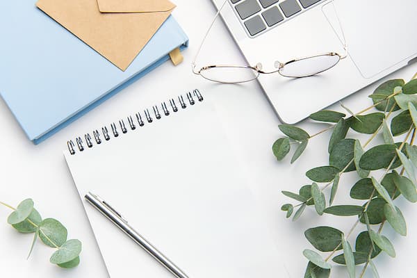 A laptop, eye glasses, and notebooks sitting on a white desk.