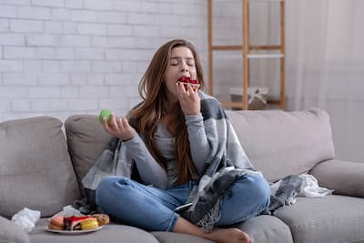 Sad teen girl eating a lot of deserts on her couch